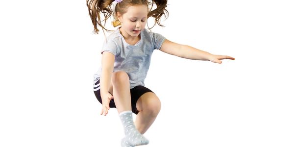 Young girl joyfully jumping mid-air with pigtails flying.