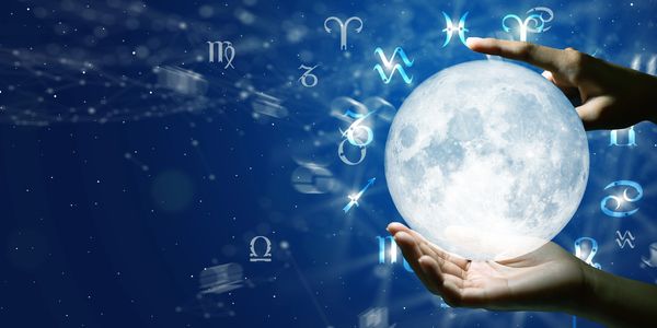 Hands holding a glowing moon surrounded by zodiac signs on a starry blue background.