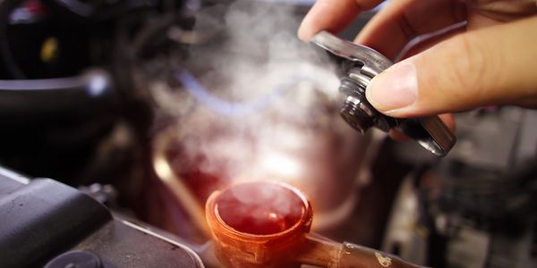 Person removing hot radiator cap with steam rising from a vehicle that needs a coolant flush and repair.