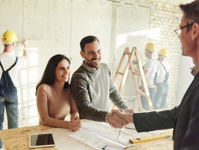 Couple shaking hands with a professional at a construction site.