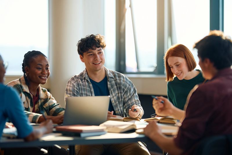 Happy college student and his friends talking while studying in the classroom.