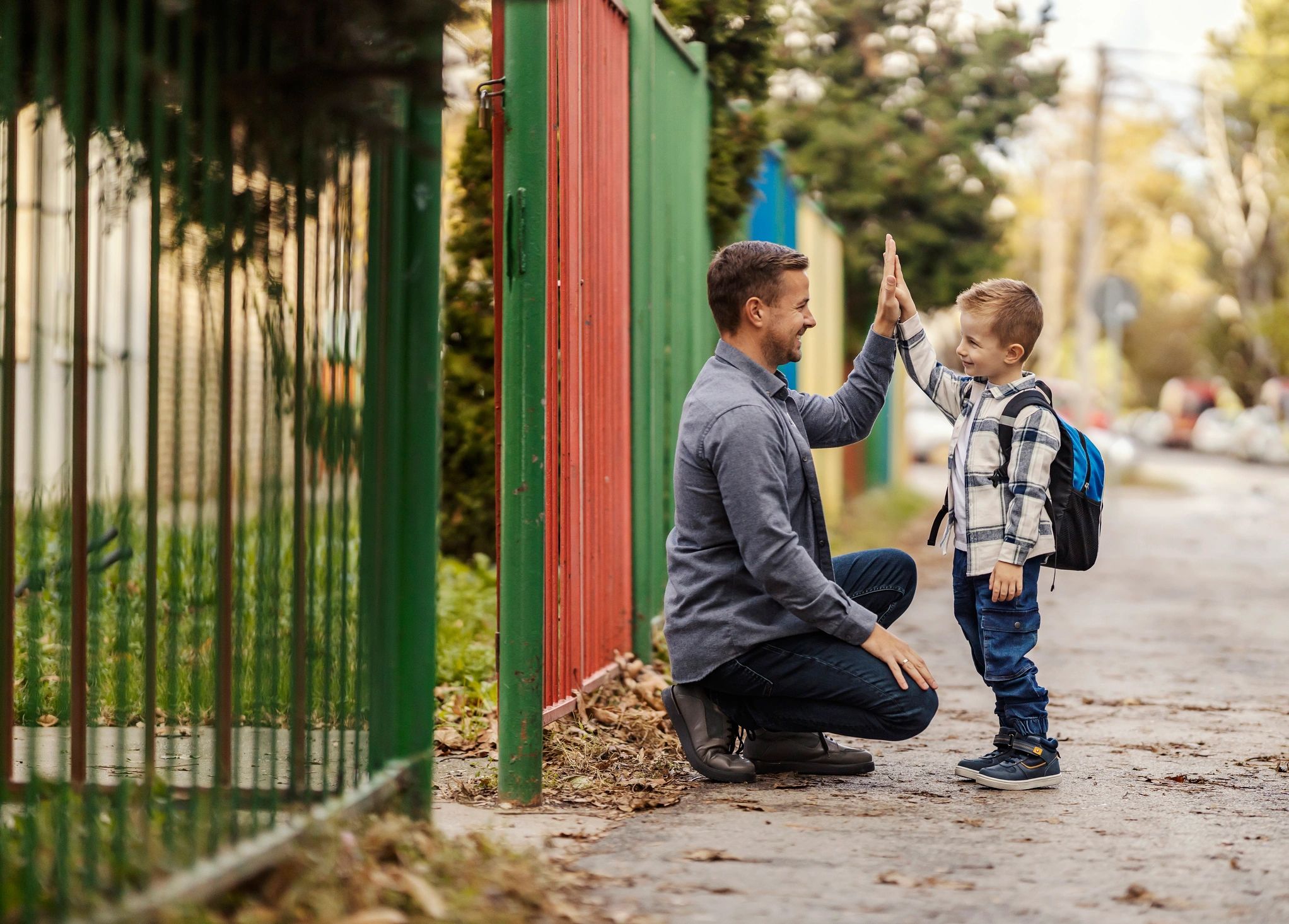 Young father kneeling down giving his small child in a checked top a high five.