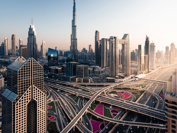 A sprawling cityscape with towering skyscrapers and intricate highway interchanges at sunset.