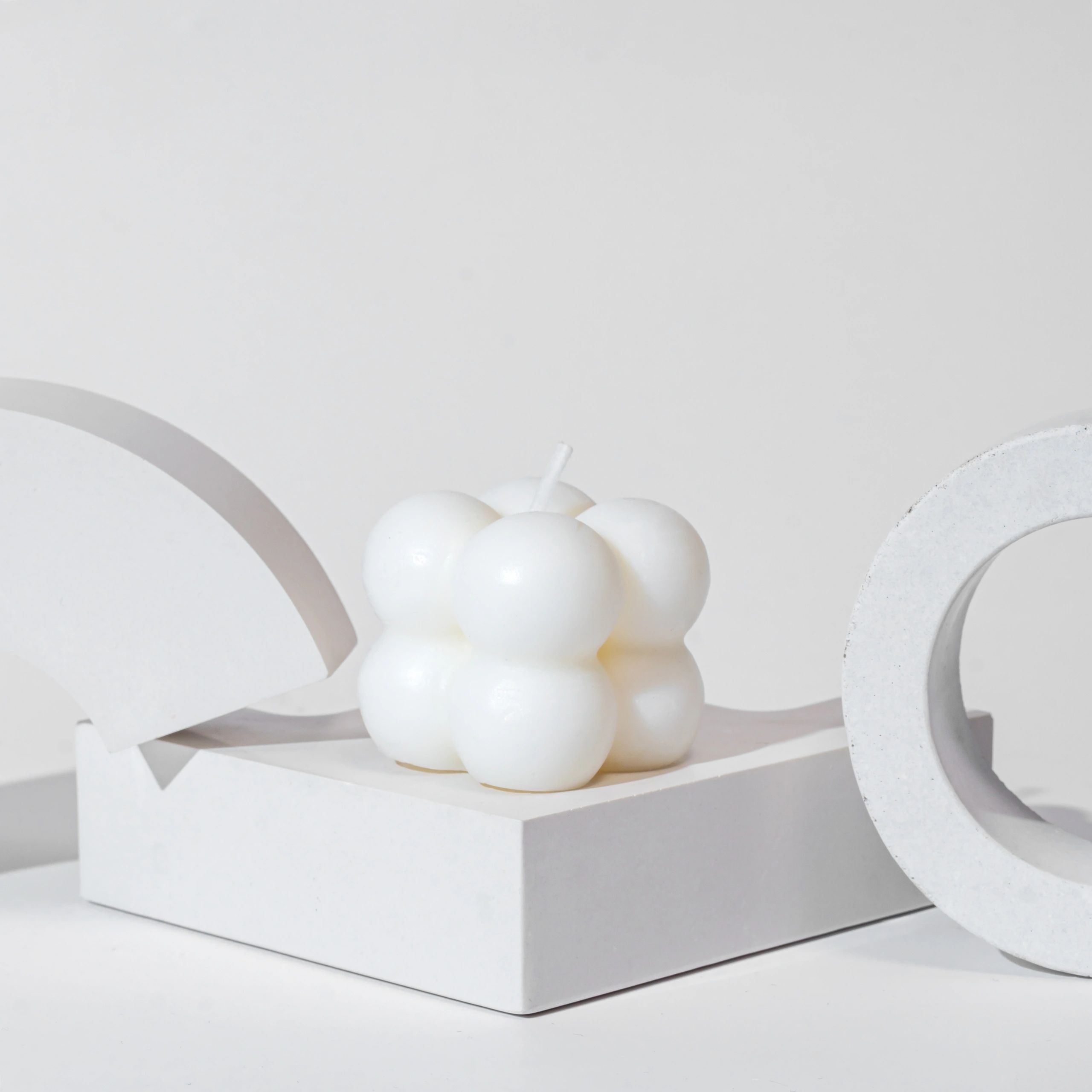 White bubble candle on a white geometric platform with abstract shapes.