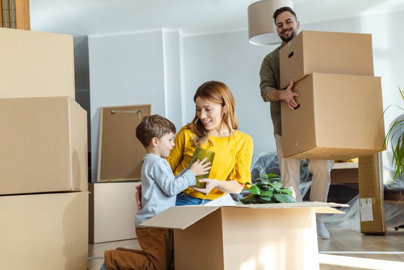Happy family with one child starting new life in new apartment. They are unpacking boxes and talking to the child while sitting on the floor