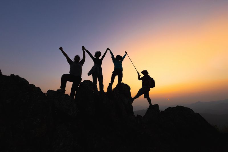 Silhouette Teamwork of four  hiker helping each other on top of mountain climbing team beautiful sunrise. Teamwork friendship hiking help each other trust assistance. climbing team success.