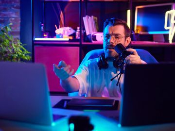 Man streaming or recording content with microphone and computer in colorful room.