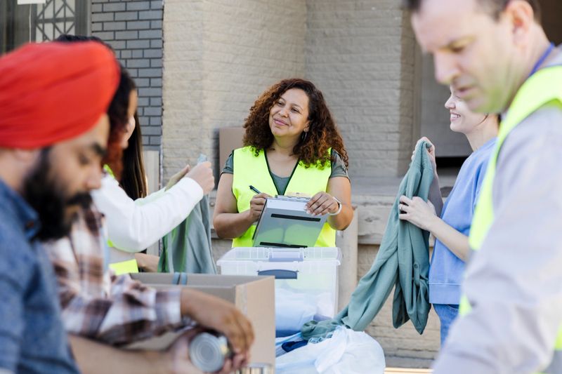 The cheerful mid adult female coordinator oversees a multiracial group of volunteers as they sort the donated food and clothing.