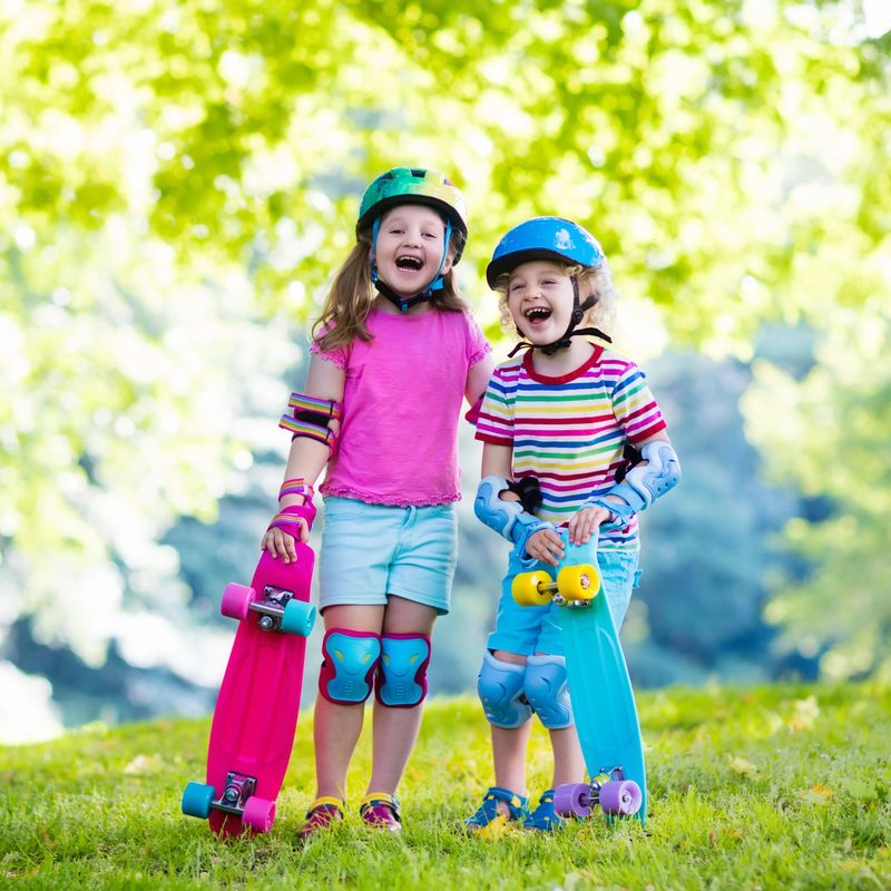 Children riding skateboard in summer park. Little girl and boy learn to ride skate board, help and support each other. Active outdoor sport for kids. Child skateboarding. Preschooler kid skating.