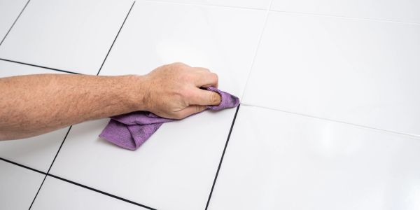 Hand cleaning tile grout with cloth.
