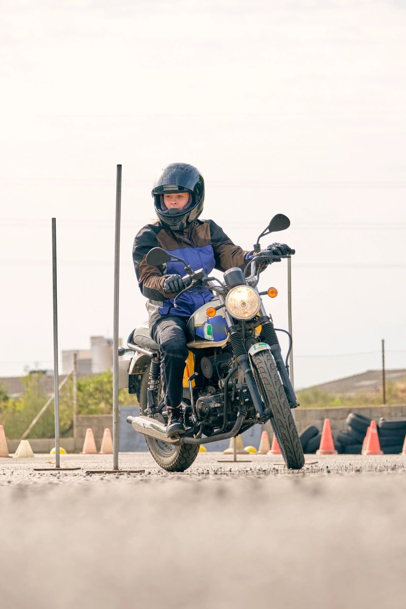 Ground level of female motorcyclist riding motorbike on asphalt motordrome with metal obstacles and oranges cones