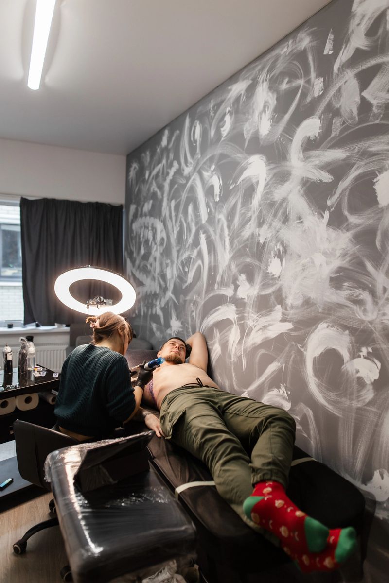 This image showcases a woman tattoo artist skillfully tattooing a detailed sketch onto a man's chest