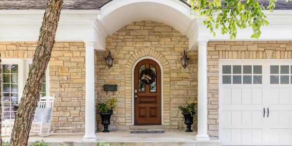 Stone house entrance with wooden door and white pillars.