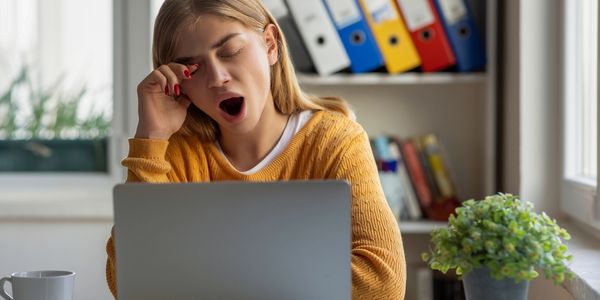 Tired young woman yawning while working on a laptop at home.