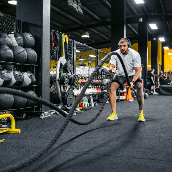 Man exercising with battle ropes in gym.