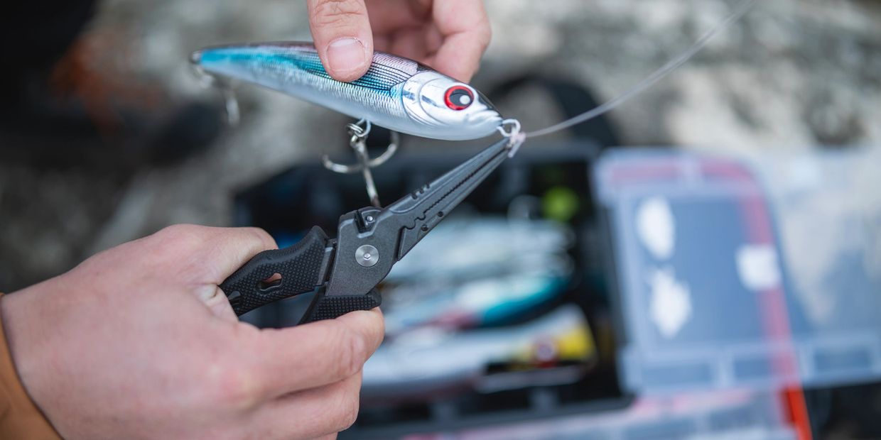 Person attaching lure to fishing line with pliers.