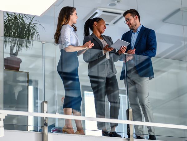 Three professionals discussing work on a tablet in a modern office.