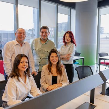 Groupe de cinq collègues souriants au bureau.