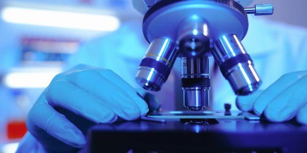 Scientist adjusting a slide on a microscope in a lab with blue lighting.