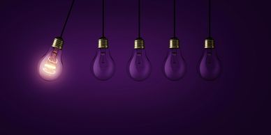 One illuminated light bulb among four unlit ones on a purple background.
