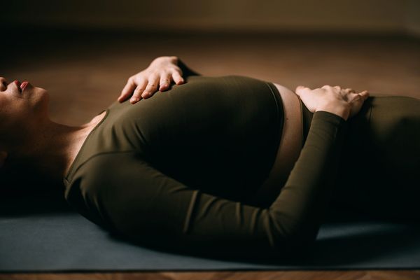 Frau entspannt auf Matte, Hände auf Bauch gelegt.