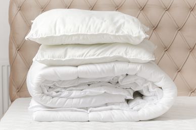 Neatly stacked white pillows and a folded comforter on a bed.