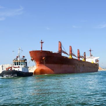 A tugboat guiding a large cargo ship in calm waters under clear skies.