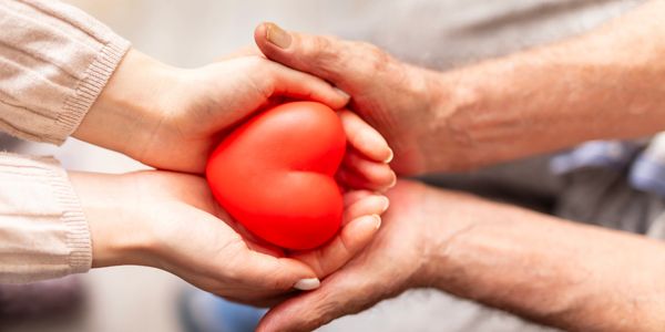 Two pairs of hands holding a red heart symbolizing love and care.