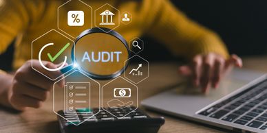 Person examining audit concepts with magnifying glass, calculator, and laptop.