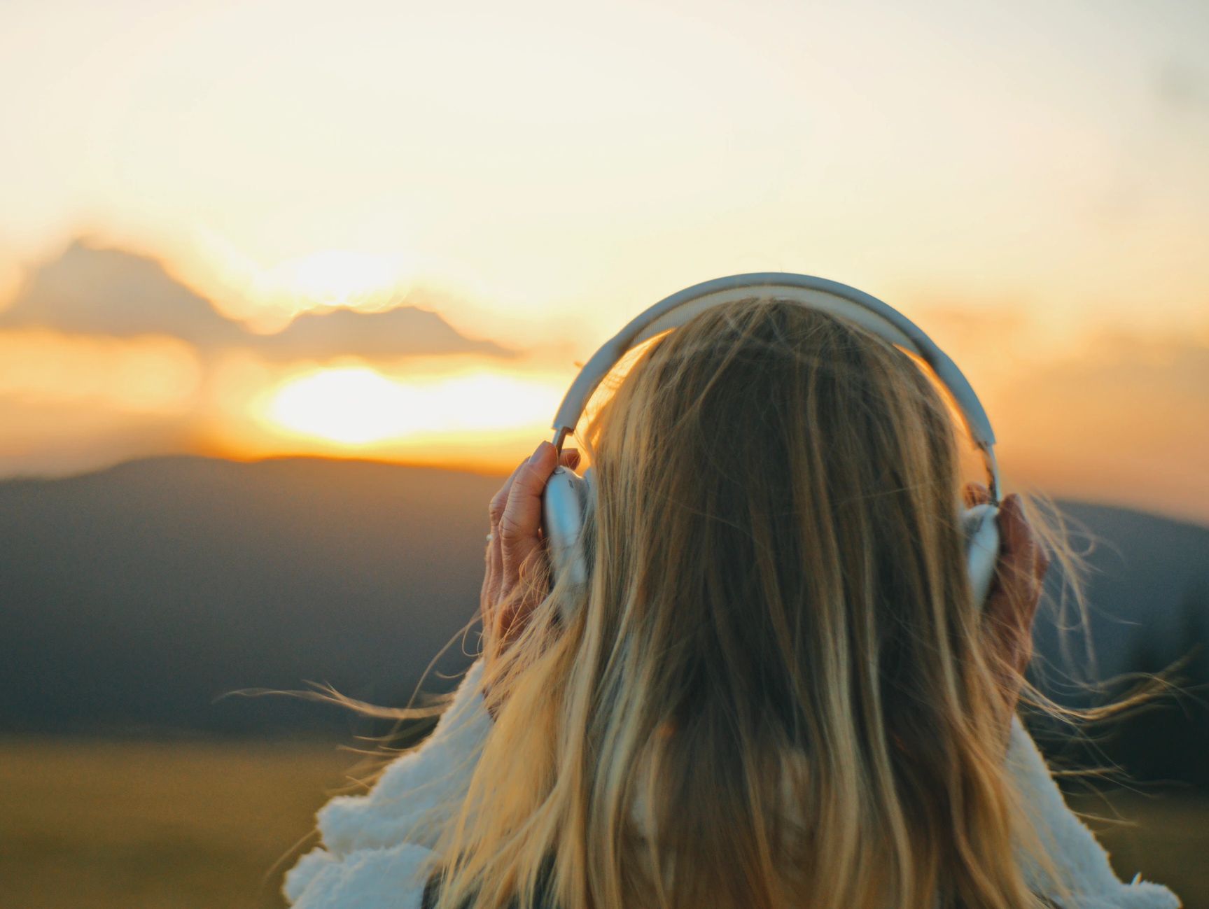 Person enjoying music with headphones at sunset in a scenic outdoor setting.