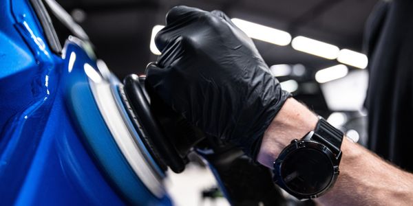 Person polishing a blue car with a buffer.