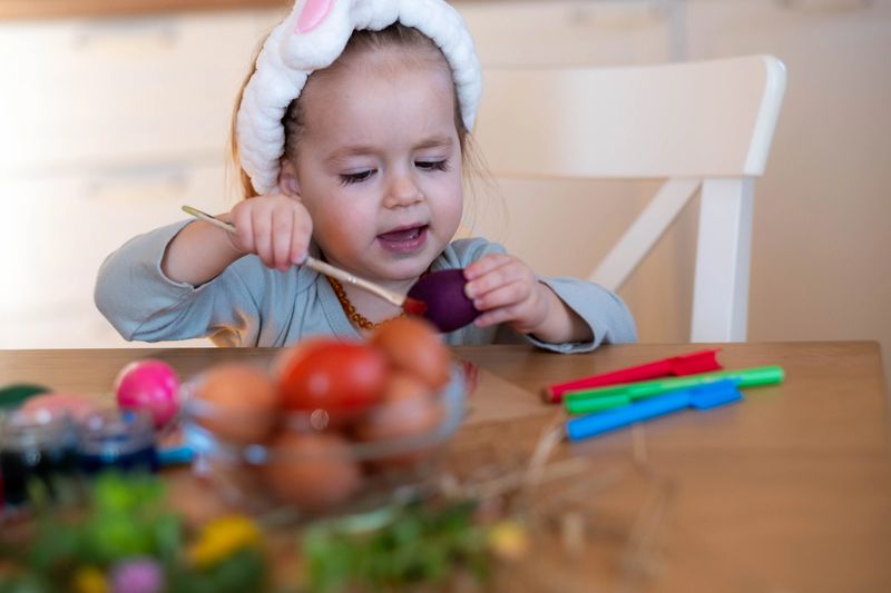 portrait of a little girl in an apartment coloring Easter eggs with an Easter scarf on her head, she is happy