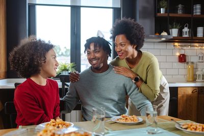 A family of 3 sitting at a table. The parents look at the daughter and smile.