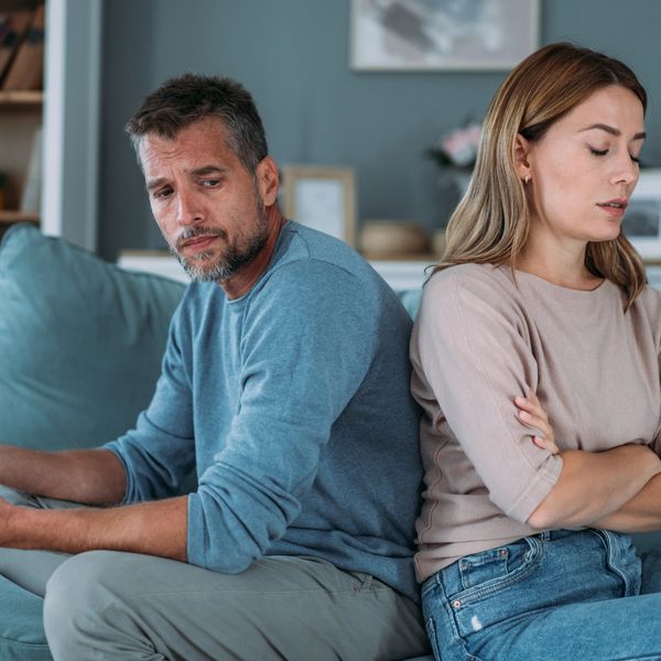 Couple sitting back-to-back on a couch, appearing upset and distant.