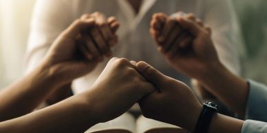 People holding hands in prayer over an open book.