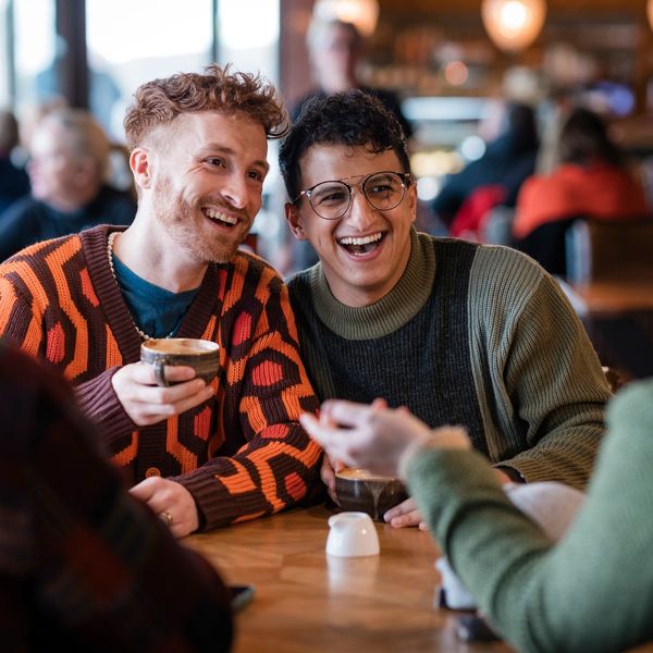 Two men laughing and enjoying coffee at a cozy café with friends.