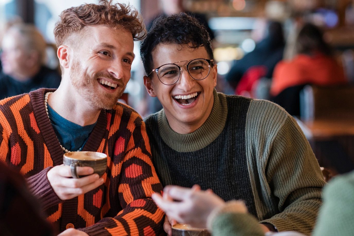 Two men laughing and enjoying coffee at a cozy café with friends.