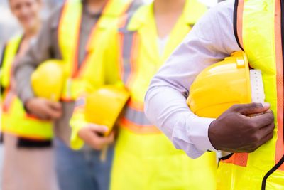 Construction workers holding yellow safety helmets, wearing reflective vests.