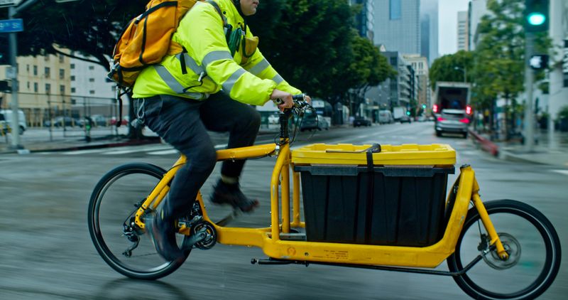 A cargo bike delivery person riding their bike on the streets of downtown Los Angeles on a rainy day in winter.