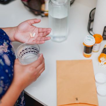 Person holding pills and a glass of water, with medication bottles on a table.