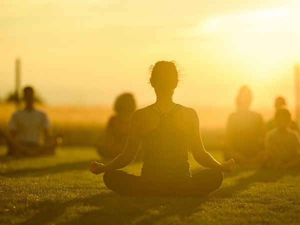 People meditating outdoors at sunset.