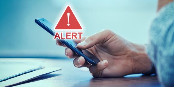 Hand holding phone with alert sign.