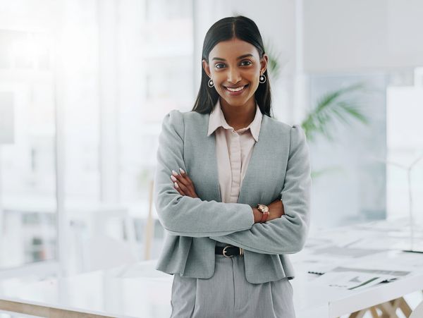 Confident businesswoman smiling with arms crossed in a bright office.