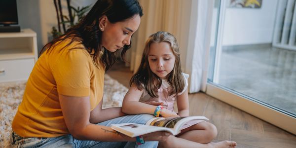 A woman reading a book with a young girl near a glass door.