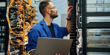 Technician inspecting server racks while holding a laptop in a data center.
