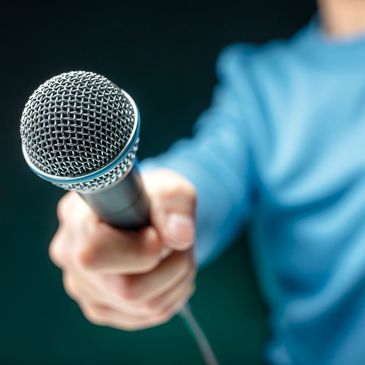 A close up of a hand and arm holding a microphone, with the mic in clear focus.