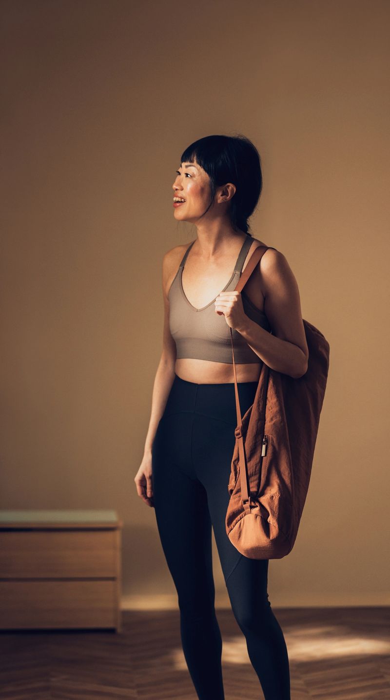 Confident female athlete holding a sports bag, dressed in activewear, preparing for a workout session in a warmly lit room.