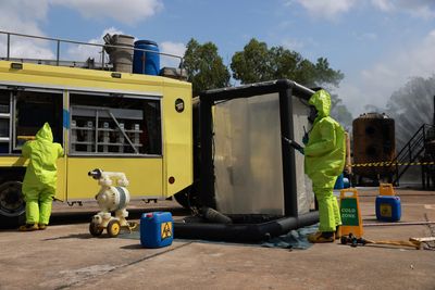 People in hazmat suits near equipment and a yellow vehicle.