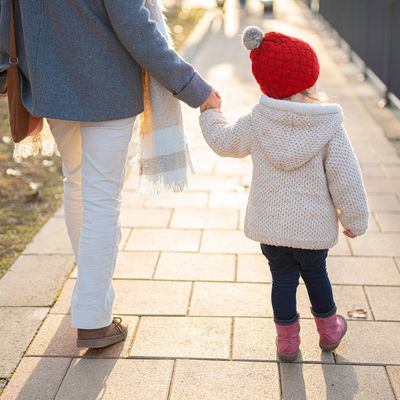 Adult and child holding hands while walking on a sunlit path.
