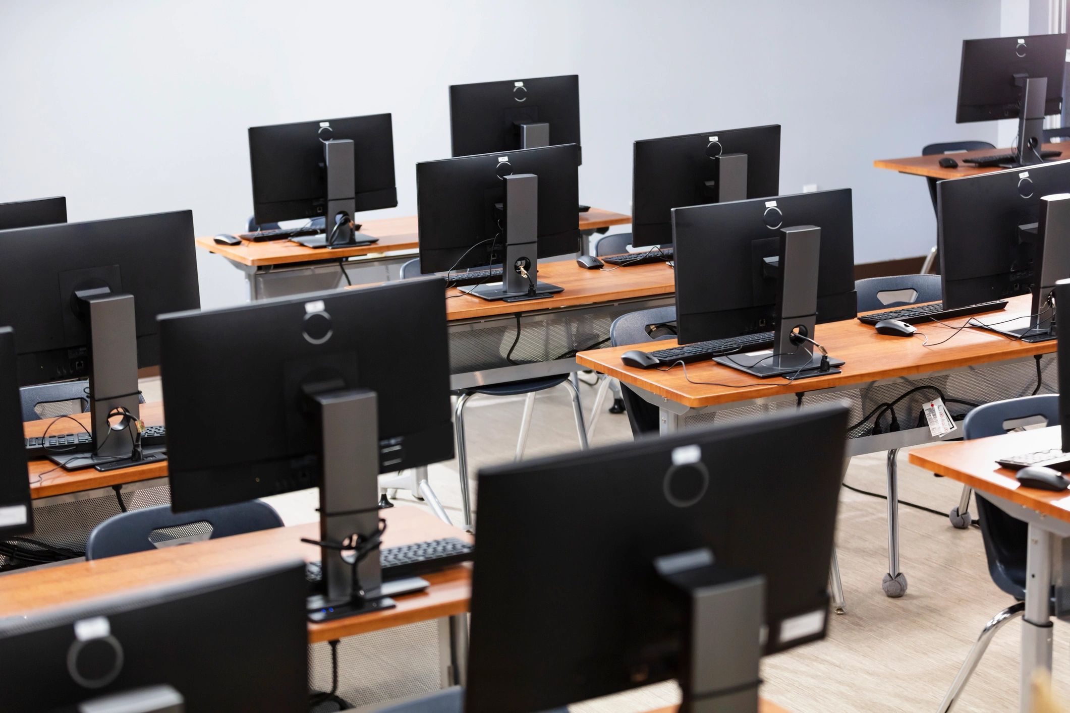 Empty computer lab with rows of monitors and keyboards on wooden desks.